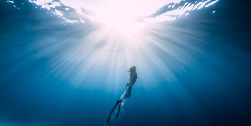 woman freediver glides over sandy sea with fins