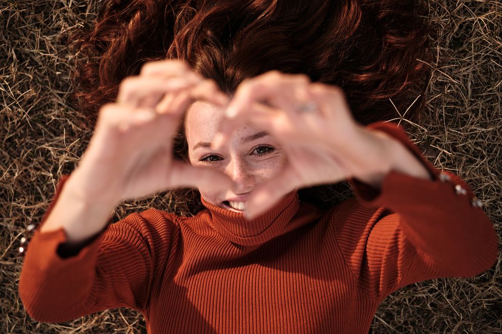 woman gesturing the shape of a heart with hands outdoors