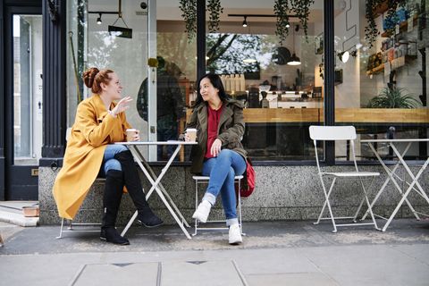 woman gesturing while talking with female friend outside coffee shop