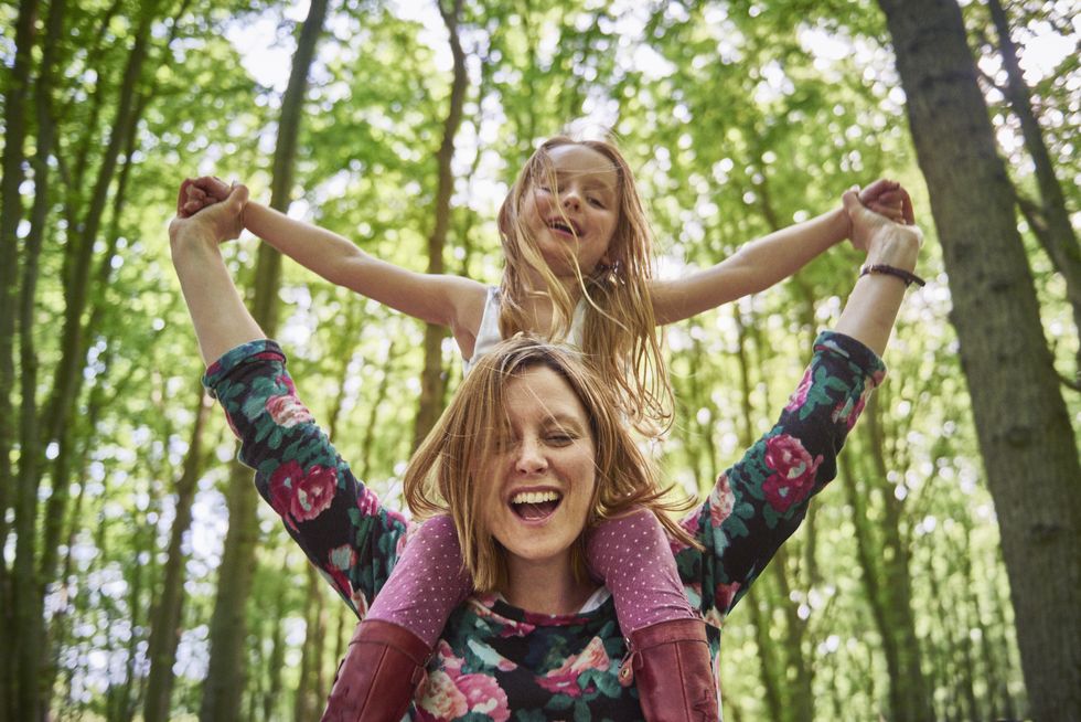 Woman giving daughter a shoulder ride in forest