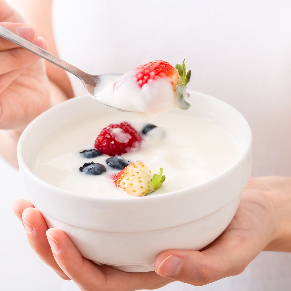 woman hand holding berry yogurt strawberry on a spoon with yogurt