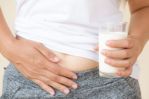 Woman hand holding glass of milk having bad stomach ache because of Lactose intolerance.