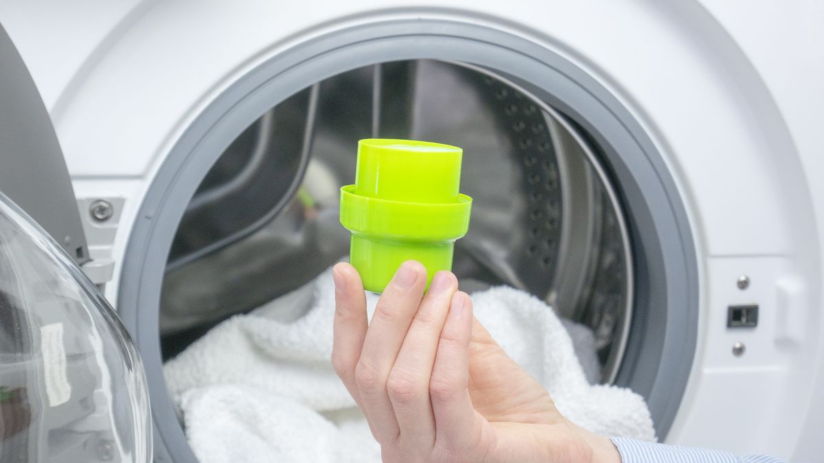 woman hand holds a measuring cap of liquid laundry detergent. open washing machine with white clothes, towels.