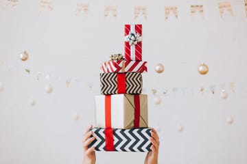 woman hands are holding stack of gift boxes with bows against white wall with garlands on strings new year celebration concept front view close up