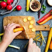 Woman hands cutting carrots on wooden board and fresh spring vegetables for vegetarian cooking on the table, top view