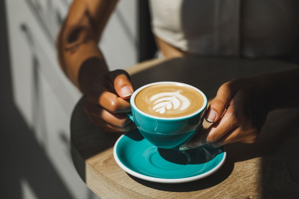 woman hands holding cup of fresh cappuccino close up beautiful natural sun light in cafe