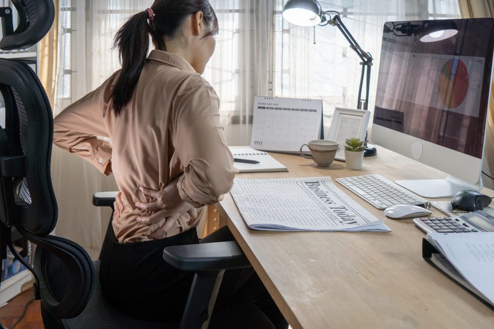 a woman has a backache while working in her home office