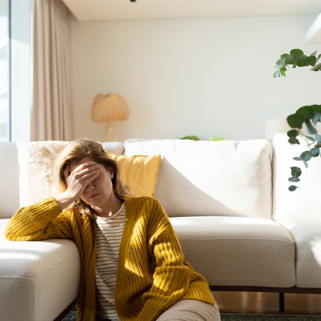 woman having headache and holding her head while sitting on the floor at home