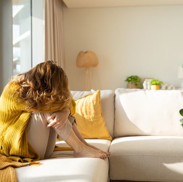 woman hiding her face while sitting on sofa at home