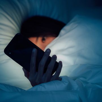 woman hiding under the blanketed and using smart phone at late night on bed