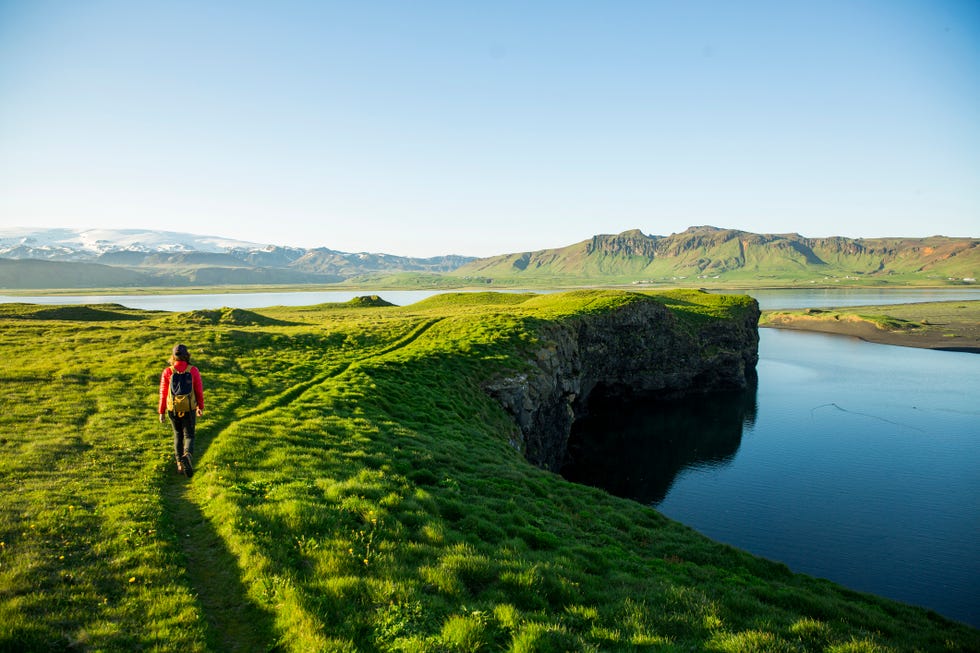 a woman hiking a lush scenic trail along a lagoon in iceland