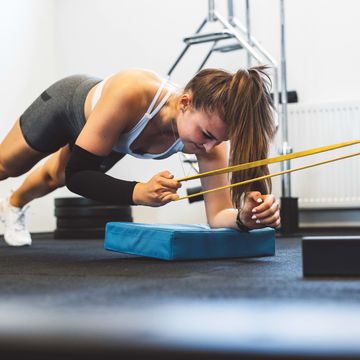 woman holding a plank while pulling for elastic band with the other hand