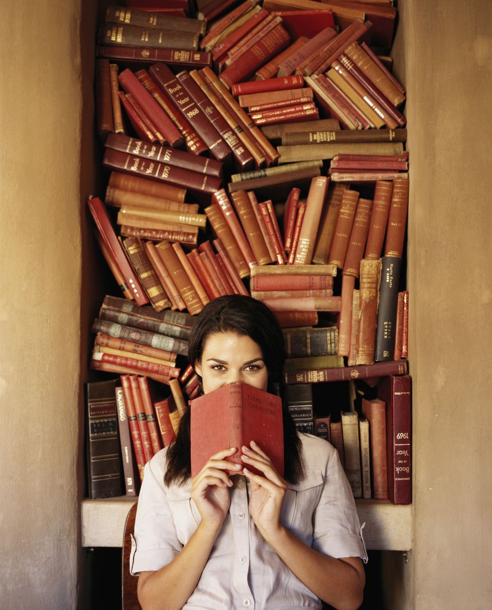 Woman holding book up to face, jumbled books in background, portrait