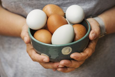 a woman holding bowl with fresh brown and white eggs