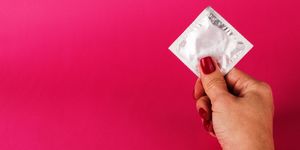 Woman holding condom on the pink background. Sex protection concept