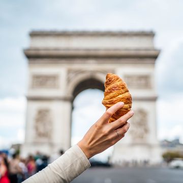 woman holding croissant in front of the famous arc de triomphe
