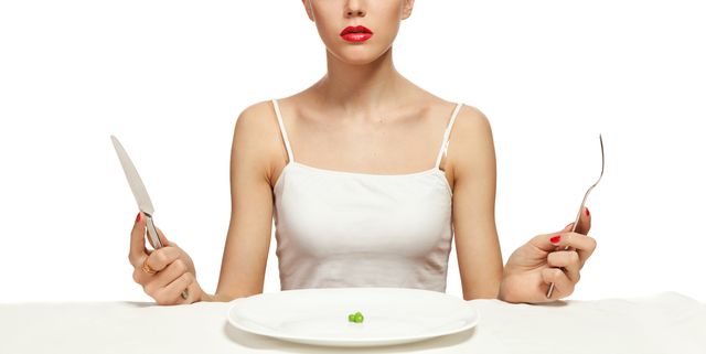 woman holding cutlery and a white plate with a single pea