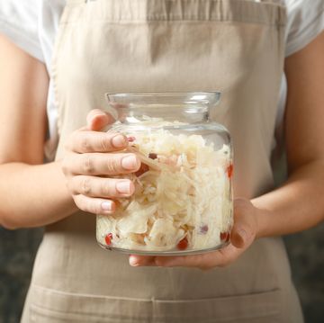 Woman holding glass jar with homemade sauerkraut on dark background, closeup