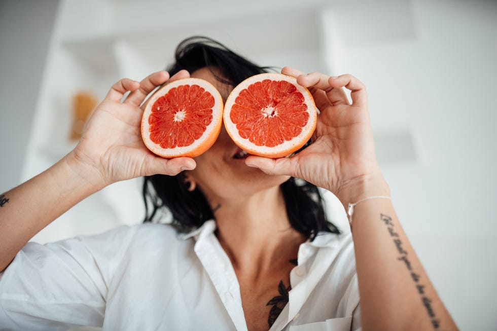 mujer sosteniendo dos rodajas de pomelo delante de sus ojos