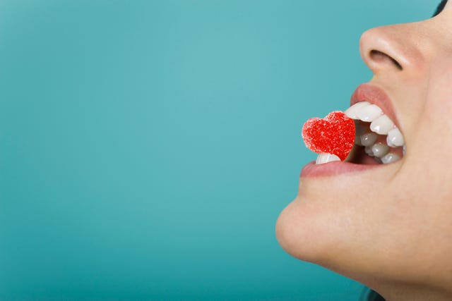 woman holding heart shaped candy between teeth, cropped