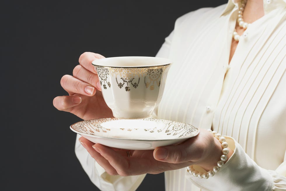 Woman holding ornate gold plated teacup and saucer