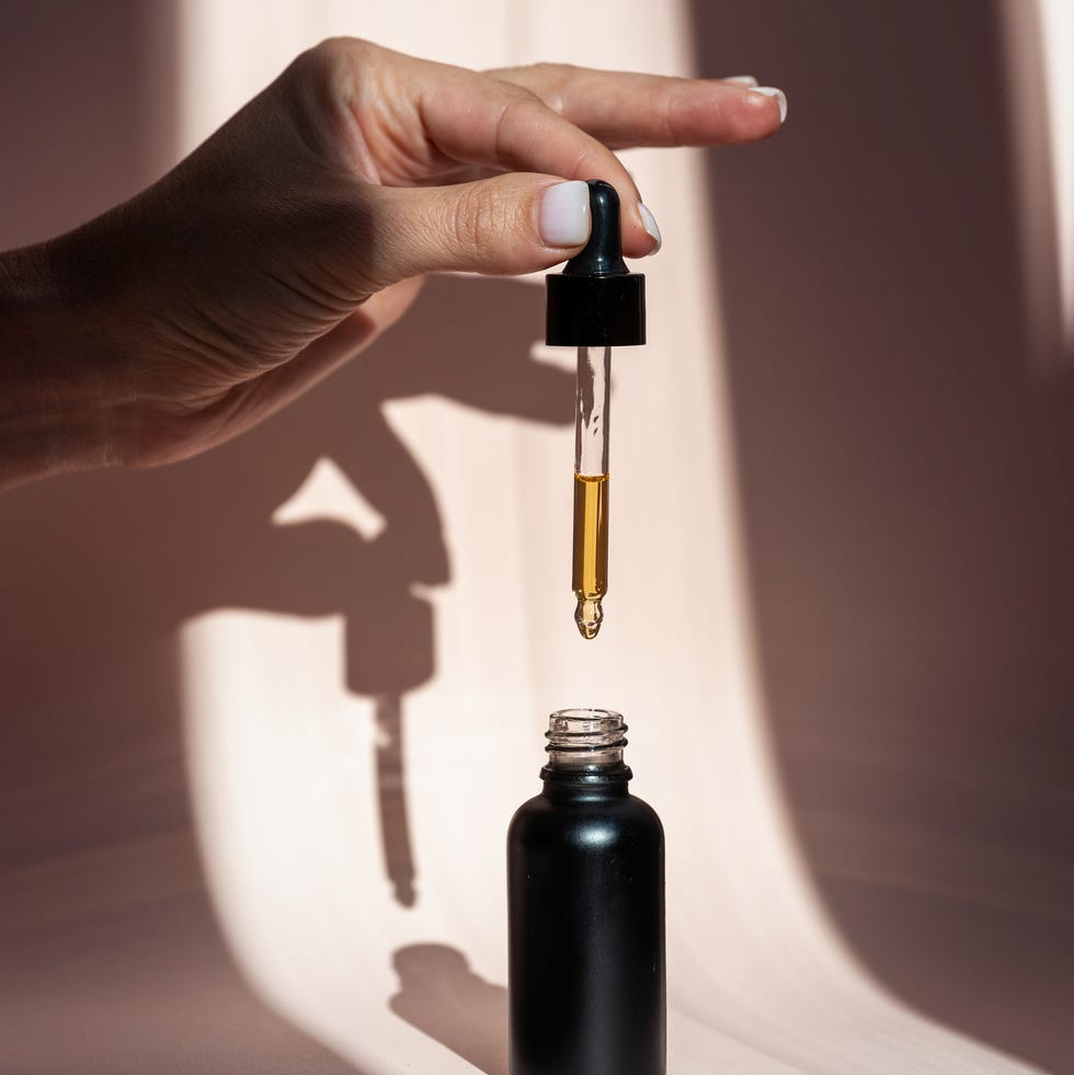 woman holding pipette with natural oil over glass bottle