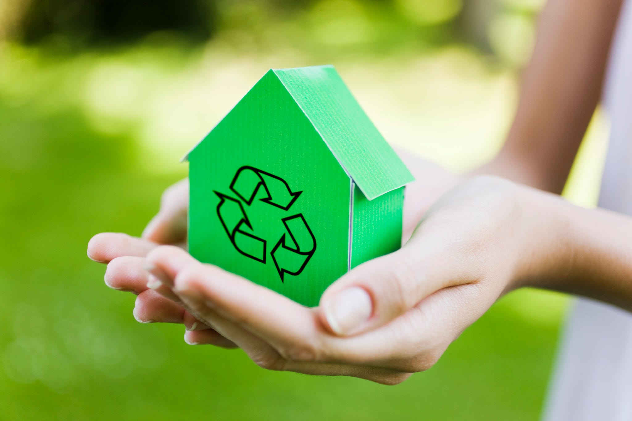 Young woman holding green model house with recycling sign