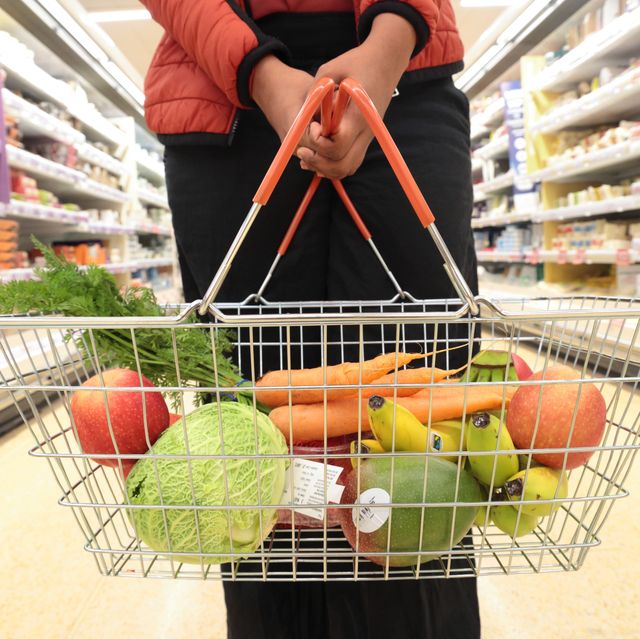woman holding shopping basket of fruit and vegetables in supermarket