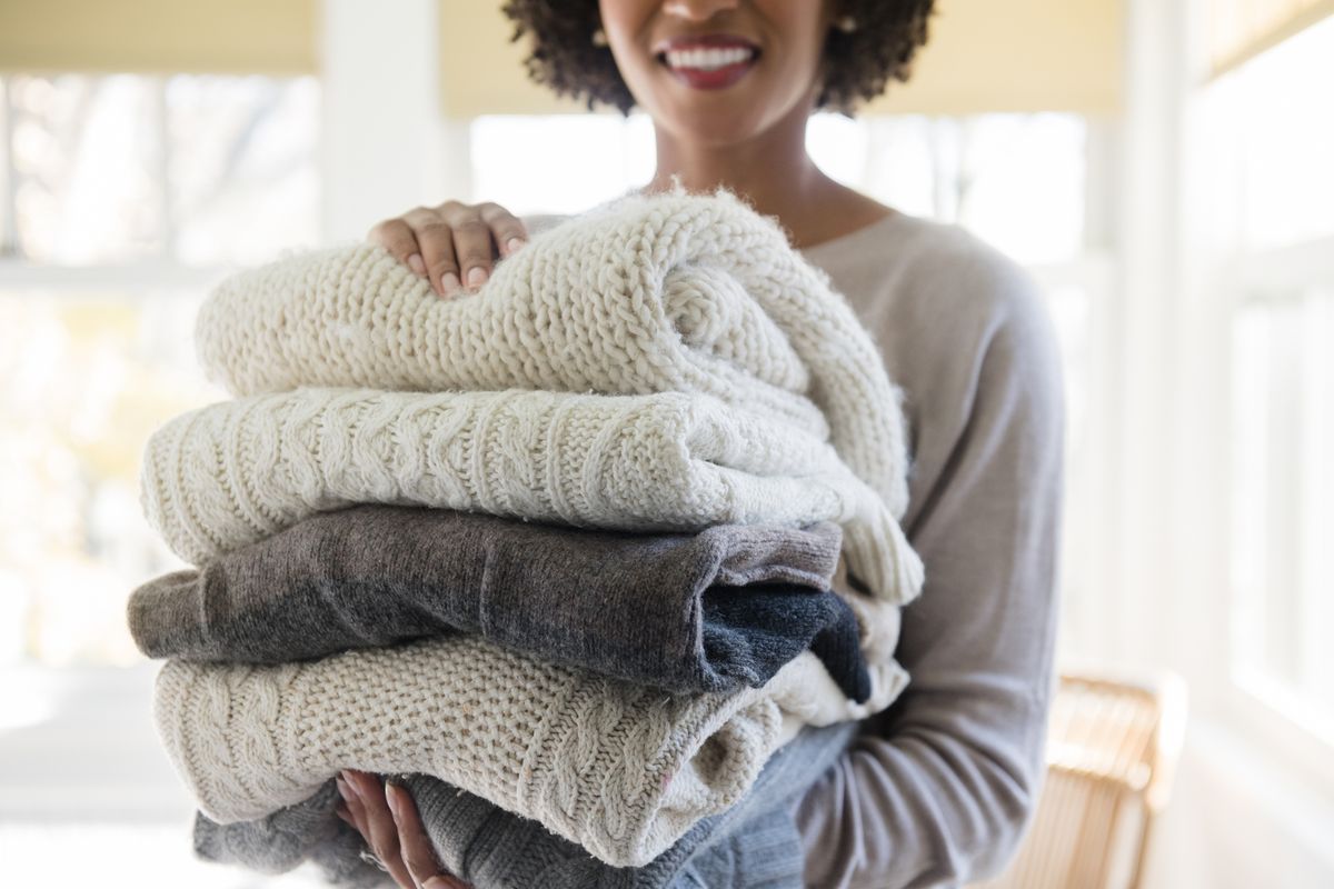 woman holding stack of folded sweaters