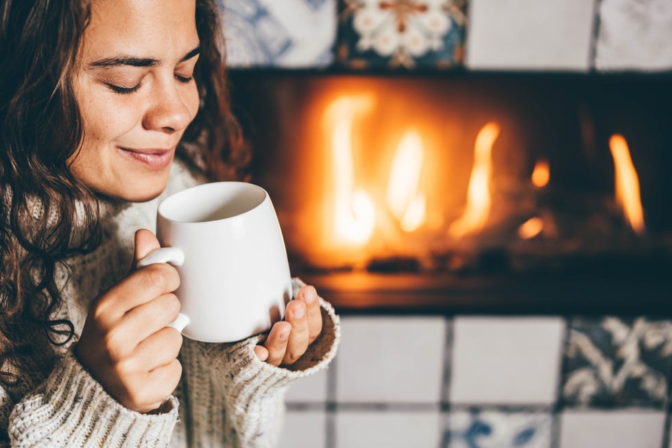 woman holding tea cup in front of fireplace at home