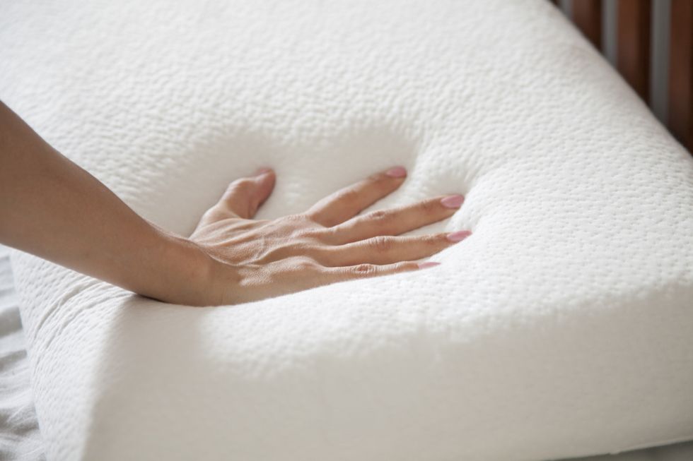 woman holding white thin memory foam pillow on white bedsheets