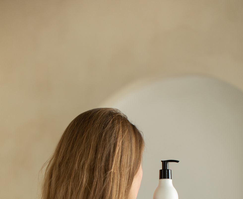 woman holds a white bottle of cosmetics in her hand, standing with her back to the camera mock up shampoo, gel
