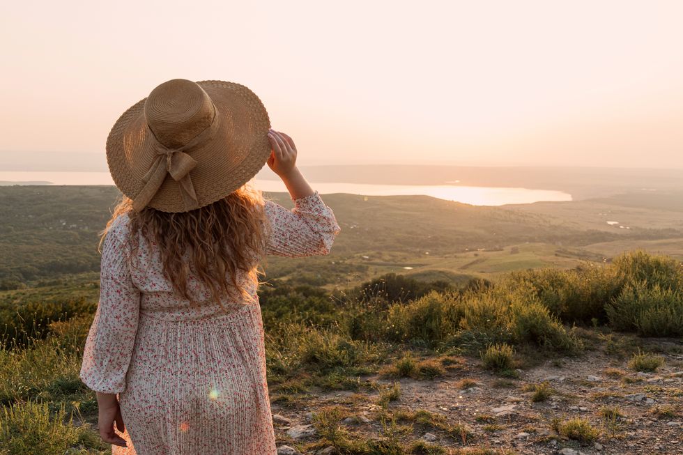 woman holds hat in her hand and watches sunset over lake selective focus picture for articles about women, success, psychology