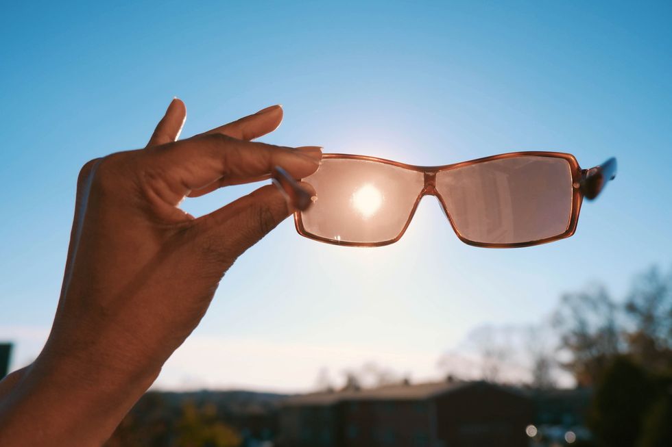 woman holds sunglasses against sky