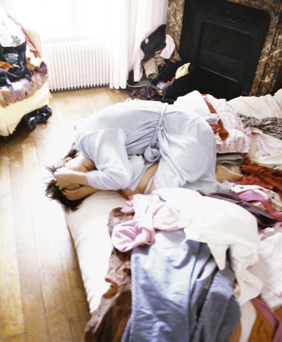 woman huddled up on bed among clothes
