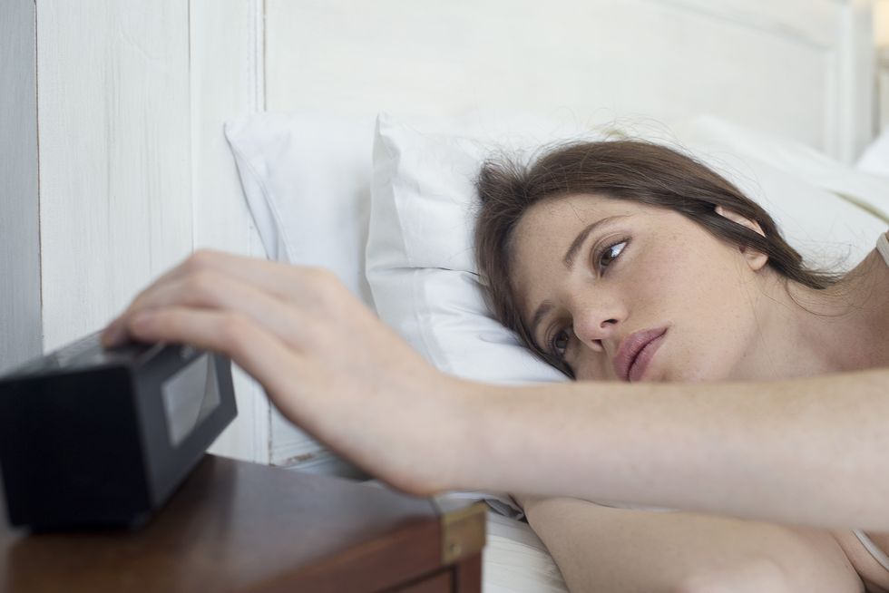 woman in bed pressing alarm clock snooze button