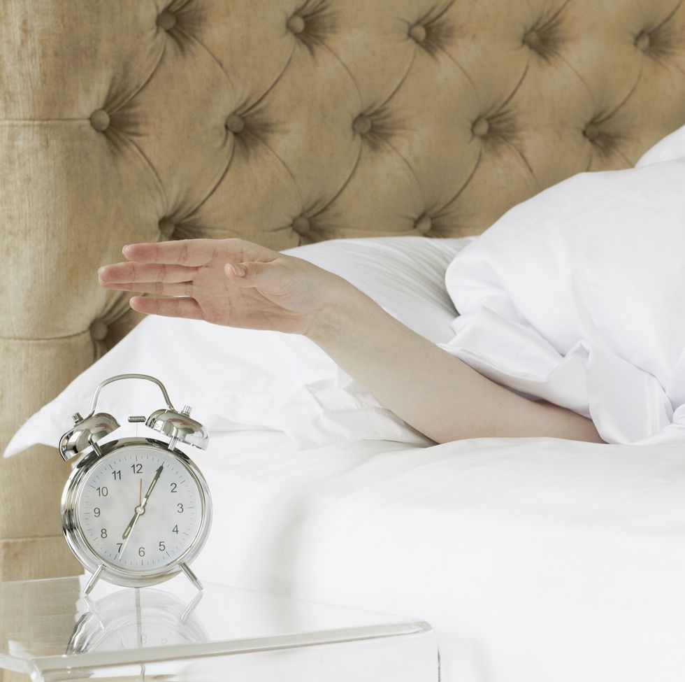woman in bed reaching out to alarm clock