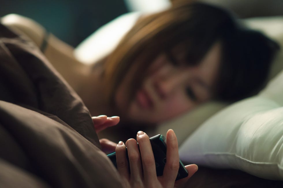 woman in bed reading smartphone