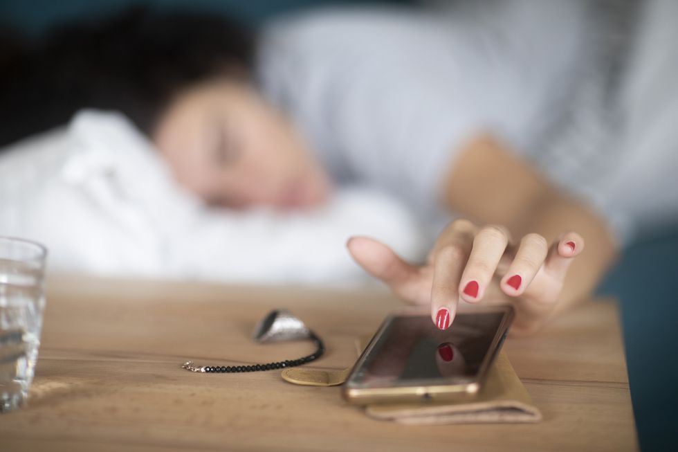 woman in bed turning off the alarm on her mobile phone
