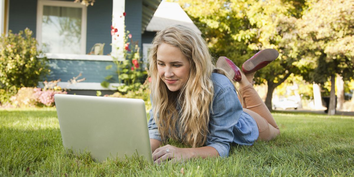 young woman lying down on grass with her laptop