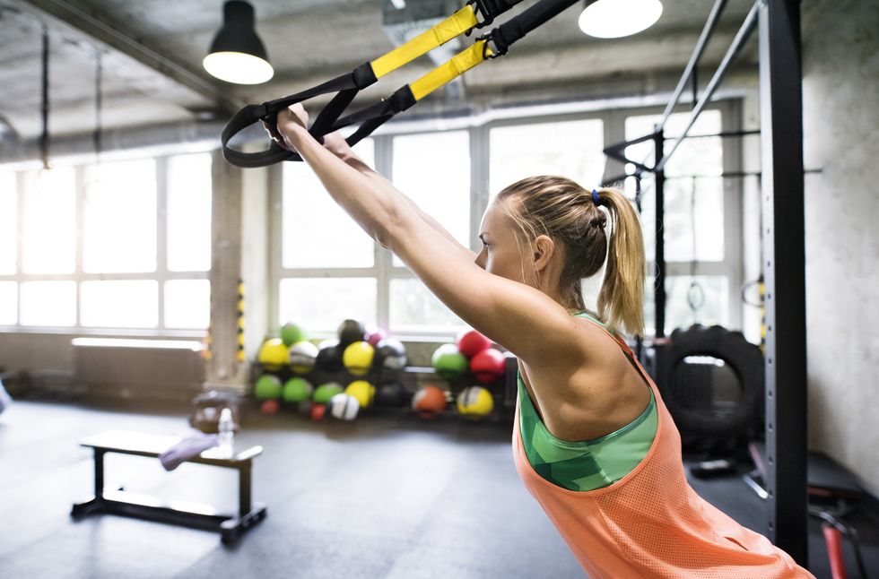 woman in gym training arms with trx fitness strips