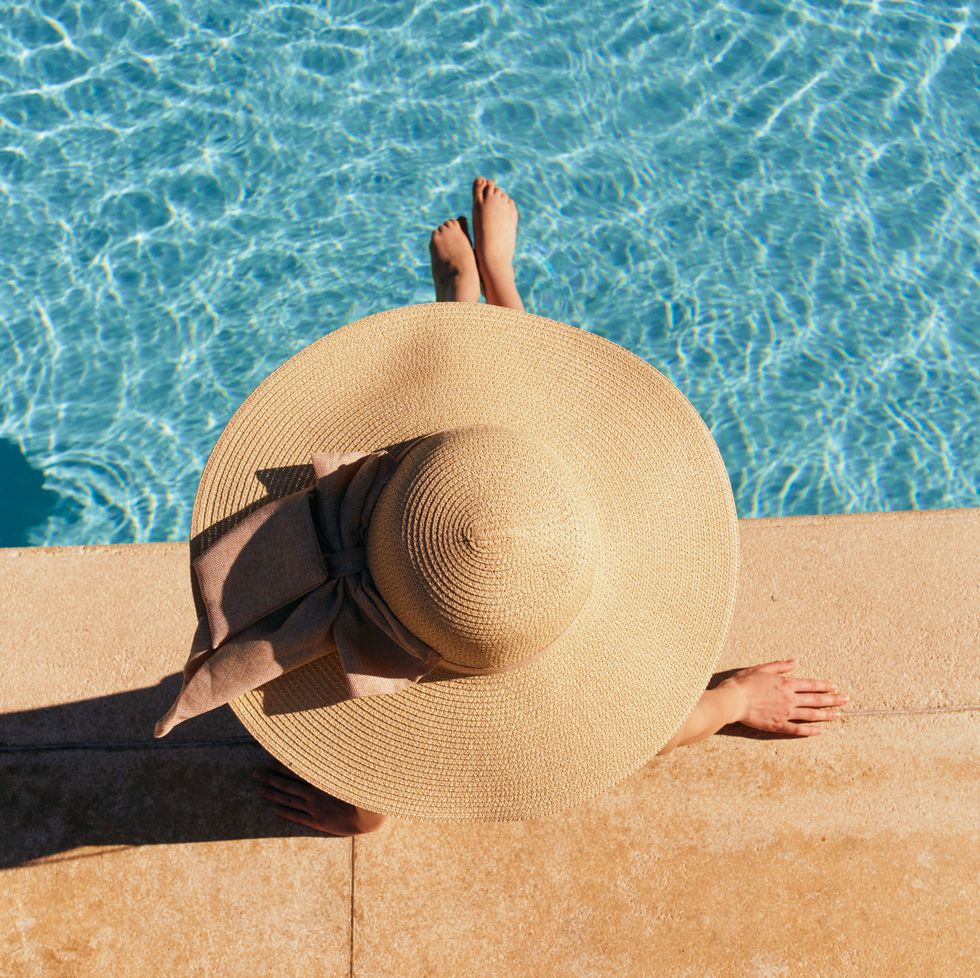 woman in hat lies near the pool, bright sun