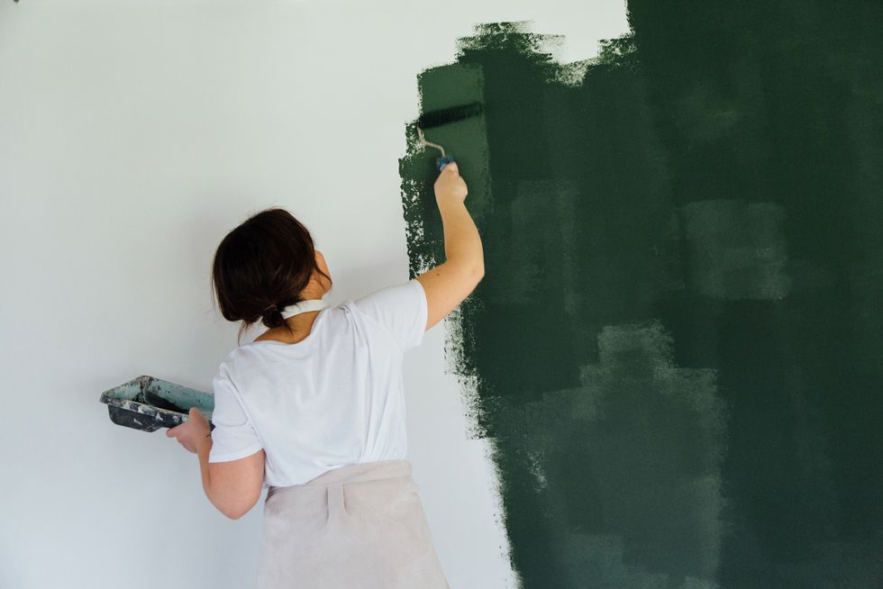 woman in head phones painting white wall in green color