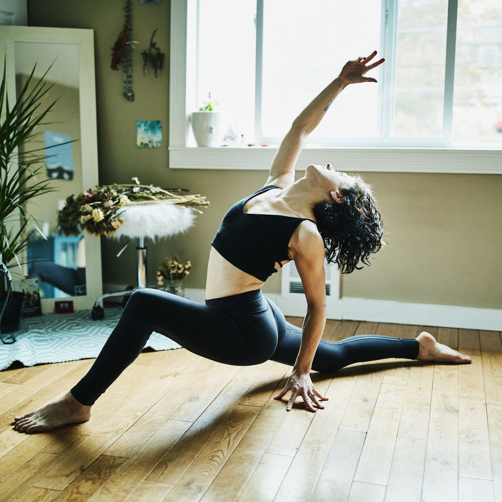 woman in low lunge with backbend pose while practicing yoga in bedroom of home