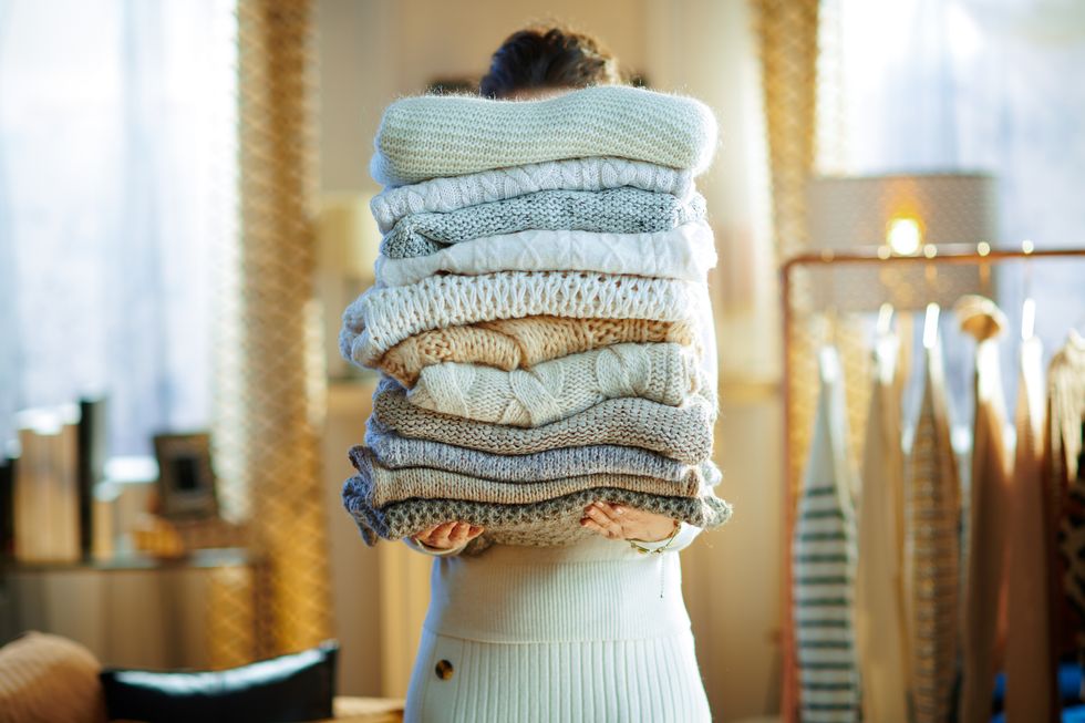 a woman holding a pile of sweaters
