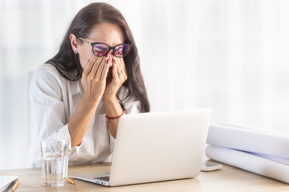 woman in the office scratches her eyes behind the eyewear as long computer work causes headache