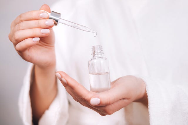 woman in white bathrobe holds serum pipette