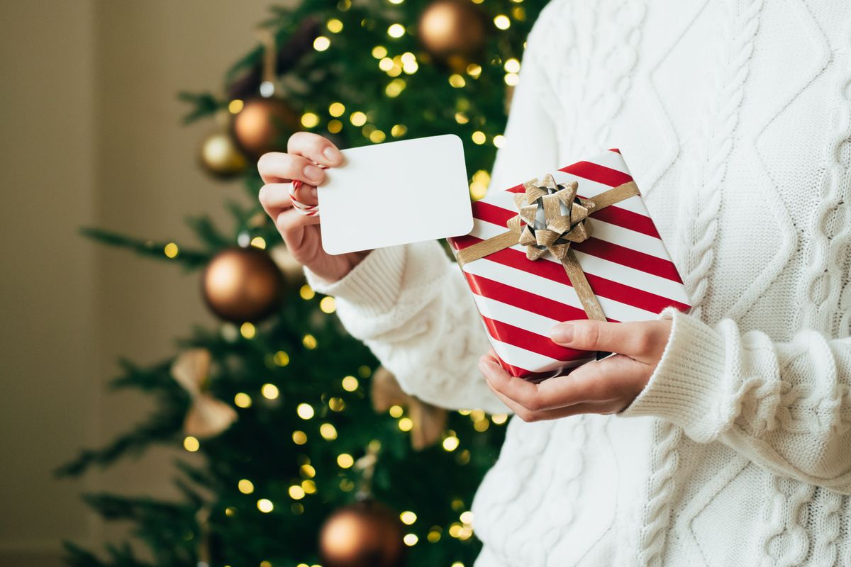 woman in white sweater is holding red white gift box