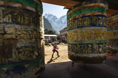a woman is hiking past prayer wheels at tengboche monastery, nepal