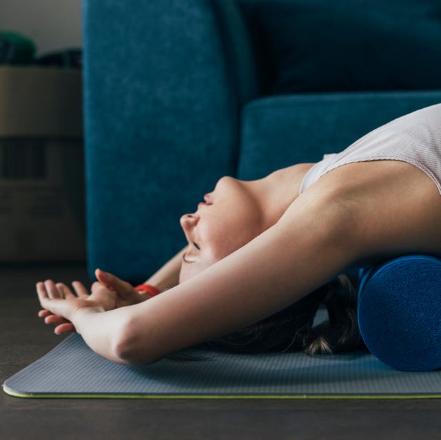 Working Out at Home: Woman is Sportswear Using a Roller to Massage Back Muscles working out at home woman is sportswear using a roller to massage back muscles